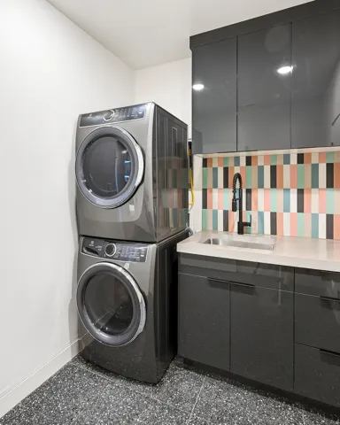Stackable washer and dryer, polished concrete countertop, integrated sink, colorful tile backsplash, and dark cabinetry