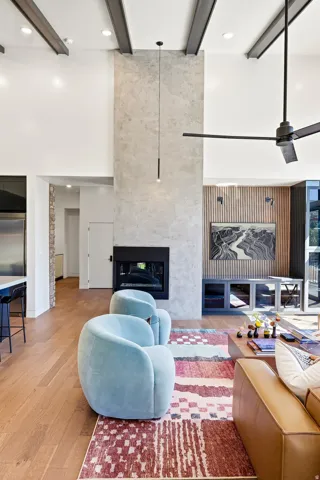 Vaulted ceilings with exposed beams, wood-finish flooring, a contemporary fireplace with a stone-finish facade, a modern pendant light fixture, and recessed lighting