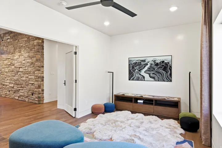 Stone accent wall, wood-finish flooring, recessed lighting, modern ceiling fan, and built-in media console