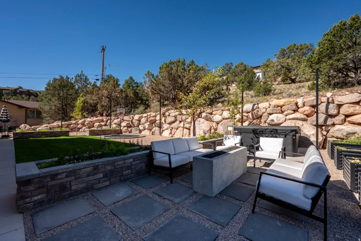 Expansive outdoor living area featuring a stone retaining wall, square paver patio, integrated fire pit, and a separate turf area