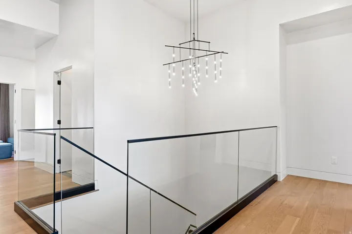 Modern chandelier, glass panel railing with black trim, wood-finish flooring, white walls, and recessed lighting