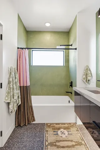 Recessed lighting illuminating a bathtub with black fixtures, set against a green textured wall and a window