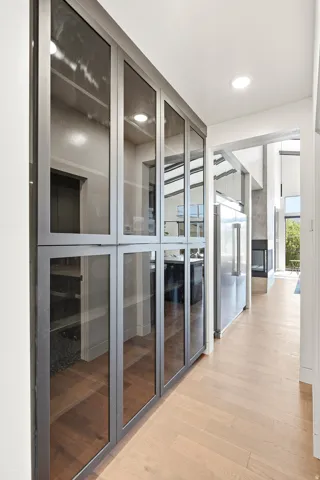 Recessed ceiling lighting, wood-finish flooring, glass-front cabinetry, stainless steel refrigerator, and a fireplace with a stone surround