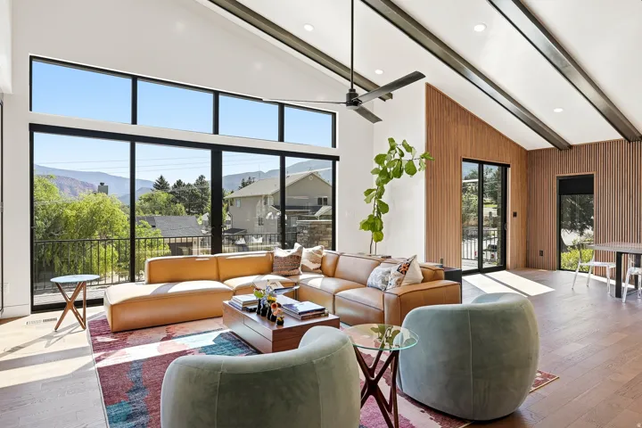 Vaulted ceilings with exposed beams, expansive floor-to-ceiling windows, wood-finish flooring, and wood slat accent walls