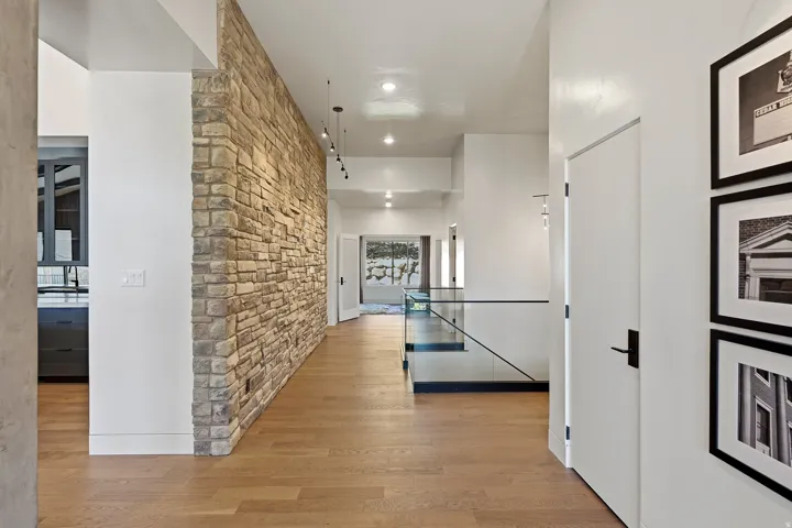 Stone accent wall, wood-finish flooring, recessed lighting, glass railing, and matte black hardware
