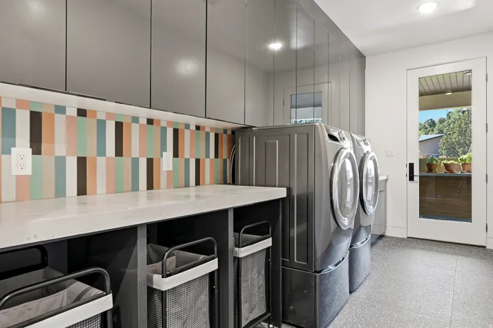 White countertop, gray cabinetry, patterned tile backsplash, and a glass-paneled door