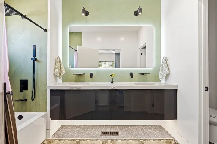 Dual vanity with an integrated countertop and undermount sinks, illuminated mirror, and matte black fixtures