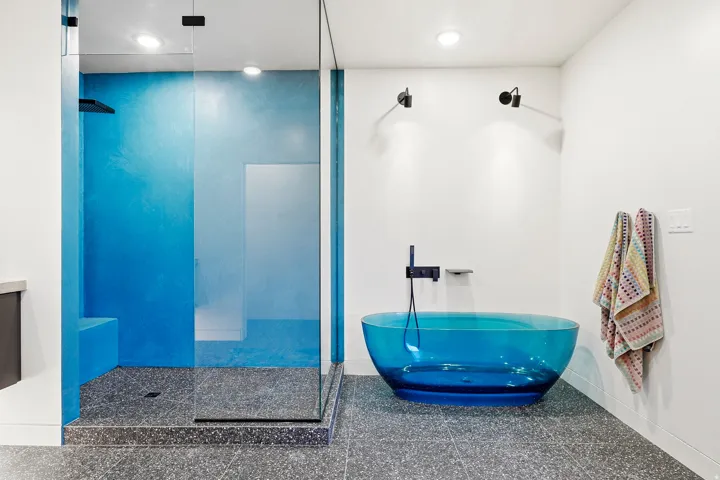Glass-enclosed shower with blue-hued walls, built-in shower bench, and dark finish rainfall showerhead