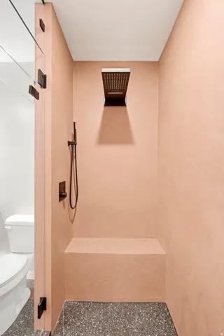 Walk-in shower with textured pink walls, black hardware, rain showerhead, built-in bench, and multi-toned flooring