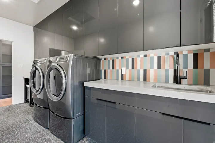 Laundry area featuring high-gloss cabinetry, a light-toned countertop with an integrated sink, a matte black faucet, and a colorful tiled backsplash