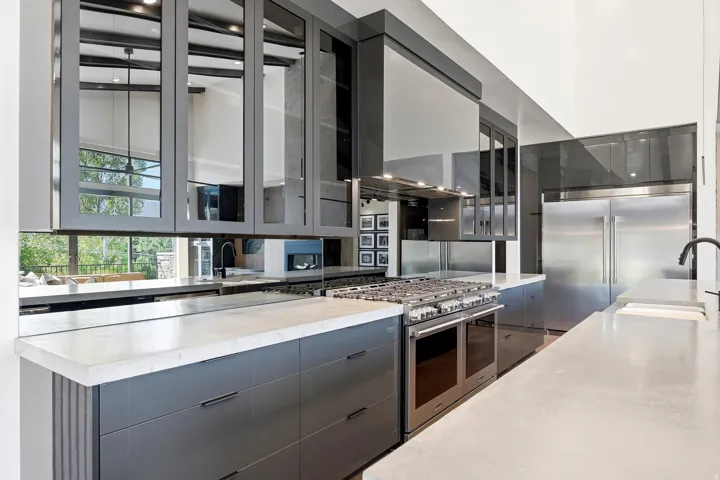 Modern kitchen featuring gray cabinetry, light-toned countertops, a stainless steel range, a stainless steel refrigerator, and mirrored upper cabinet doors