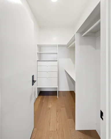 Walk-in closet featuring wood-finish flooring, built-in shelving, integrated hanging rods, and a white dresser with drawers