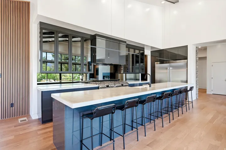 Expansive kitchen island with seating for eight, wood-finish flooring, stainless steel appliances, large windows, and high ceilings