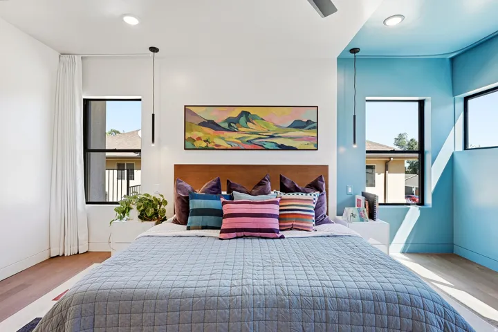 Recessed lighting, warm wood-finish flooring, multiple windows, built-in headboard, and dual pendant lights