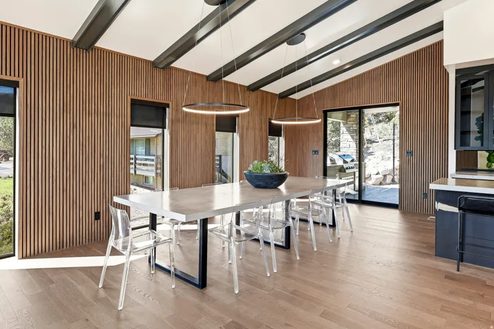 Vaulted ceiling with exposed beams, wood-panel accent wall, wood-finish flooring, sliding glass door, and built-in cabinetry with glass panels