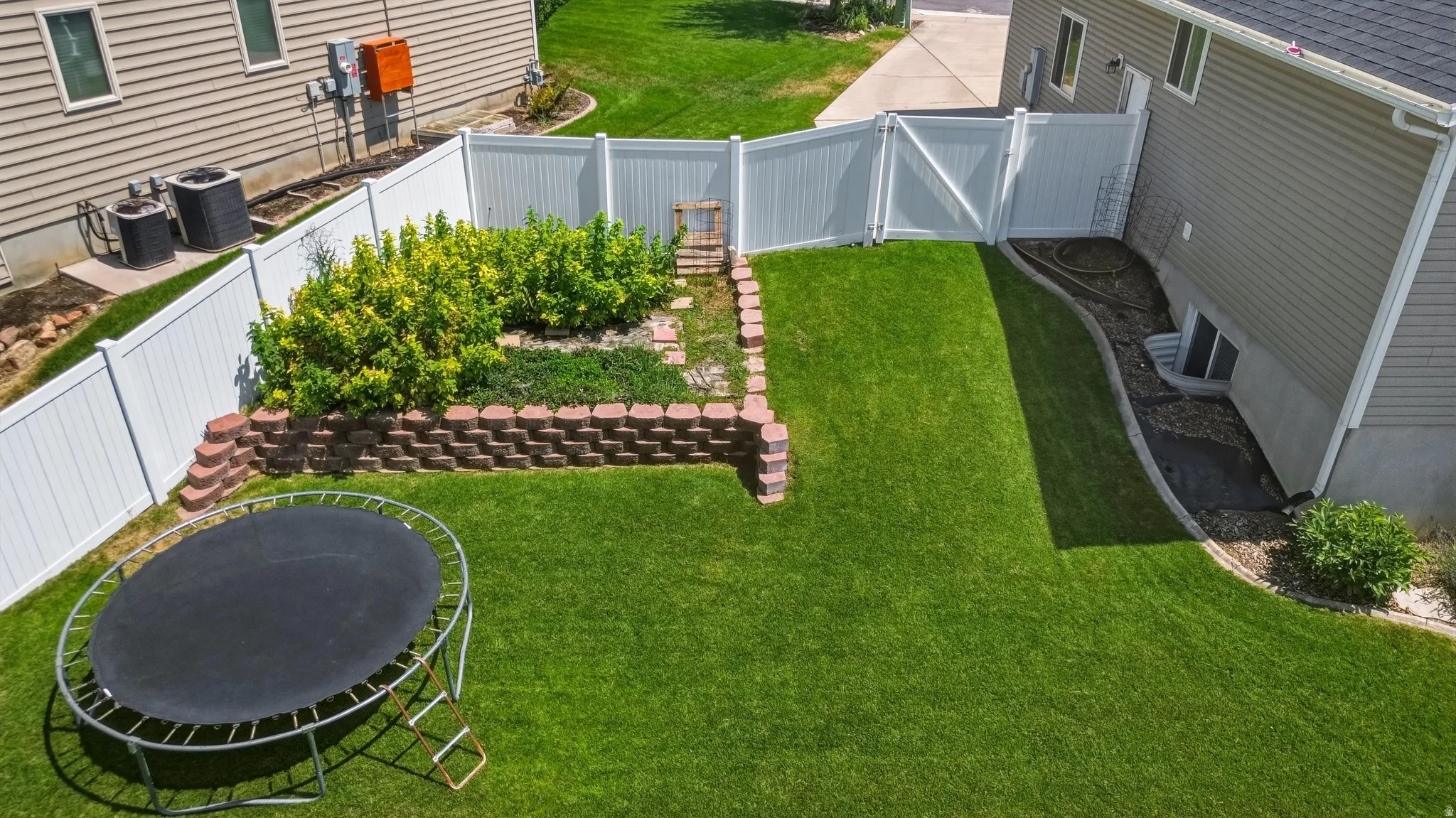 Expansive lawn area with a white privacy fence and a terraced garden bed