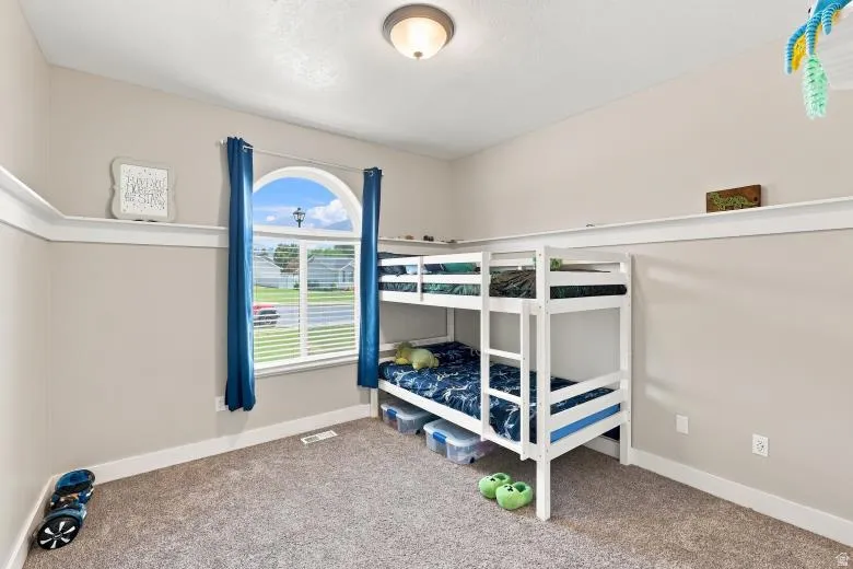 Arched window with blinds and blue drapery, wall shelving, neutral wall paint, and carpeted flooring
