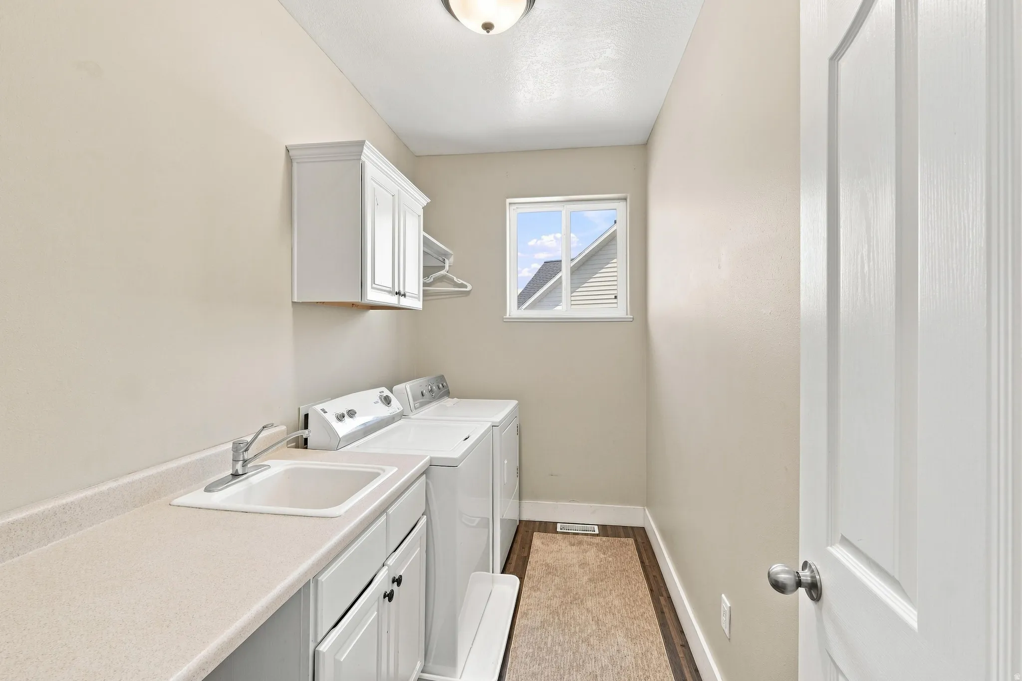 Dedicated laundry area featuring a utility sink, white cabinetry, a window, and wood-finish flooring