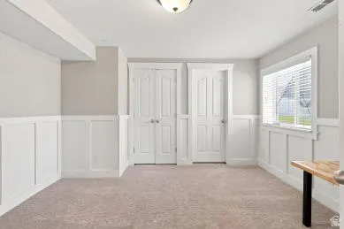Neutral wall paint, board and batten wainscoting, light-colored carpeting, white paneled doors, and a single window with blinds