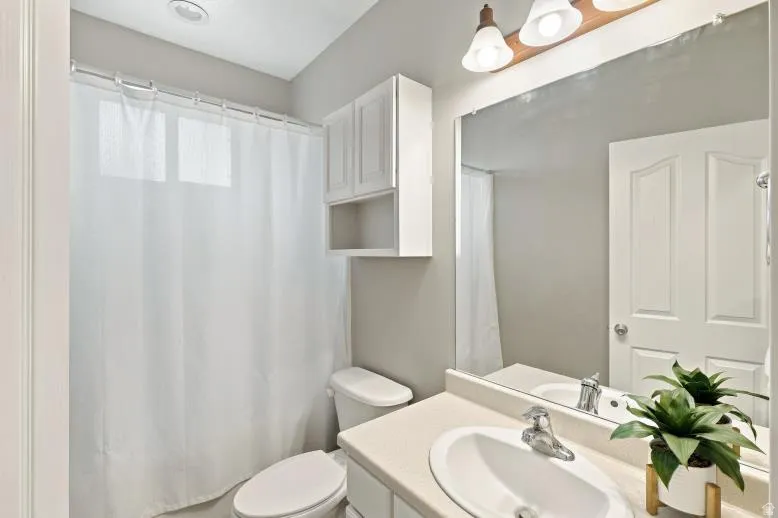 Bathroom featuring a single vanity with an integrated sink, wall-mounted mirror, overhead light fixture, toilet, and built-in white cabinetry