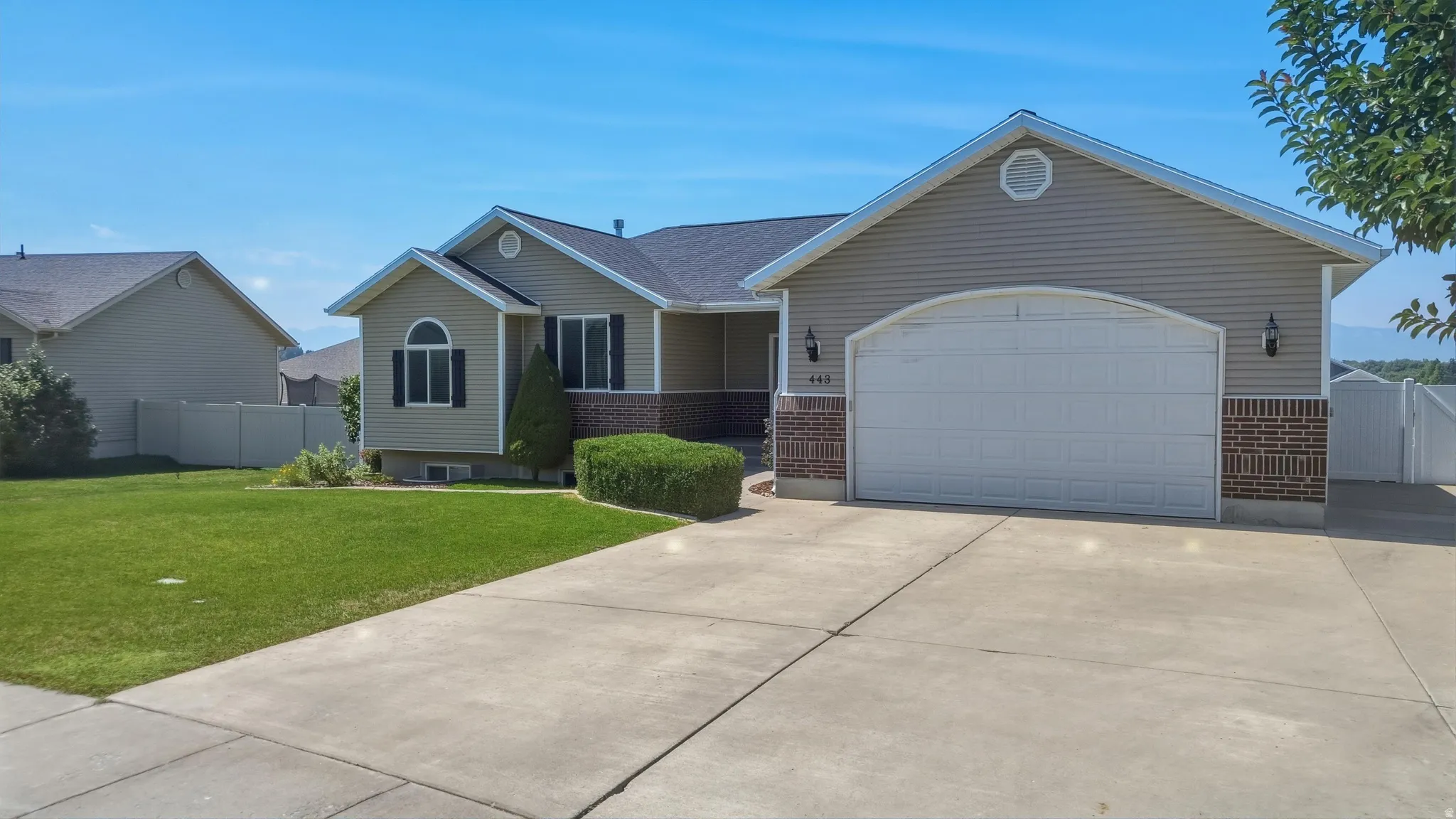 Siding exterior with brick detailing, arched garage door, concrete driveway, and mature landscaping
