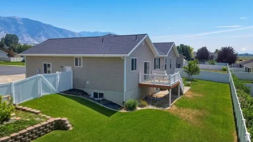 Expansive green lawn with mountain backdrop, featuring a white privacy fence and a raised wooden deck