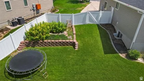Fenced backyard featuring a manicured lawn, established landscaping, and a brick retaining wall