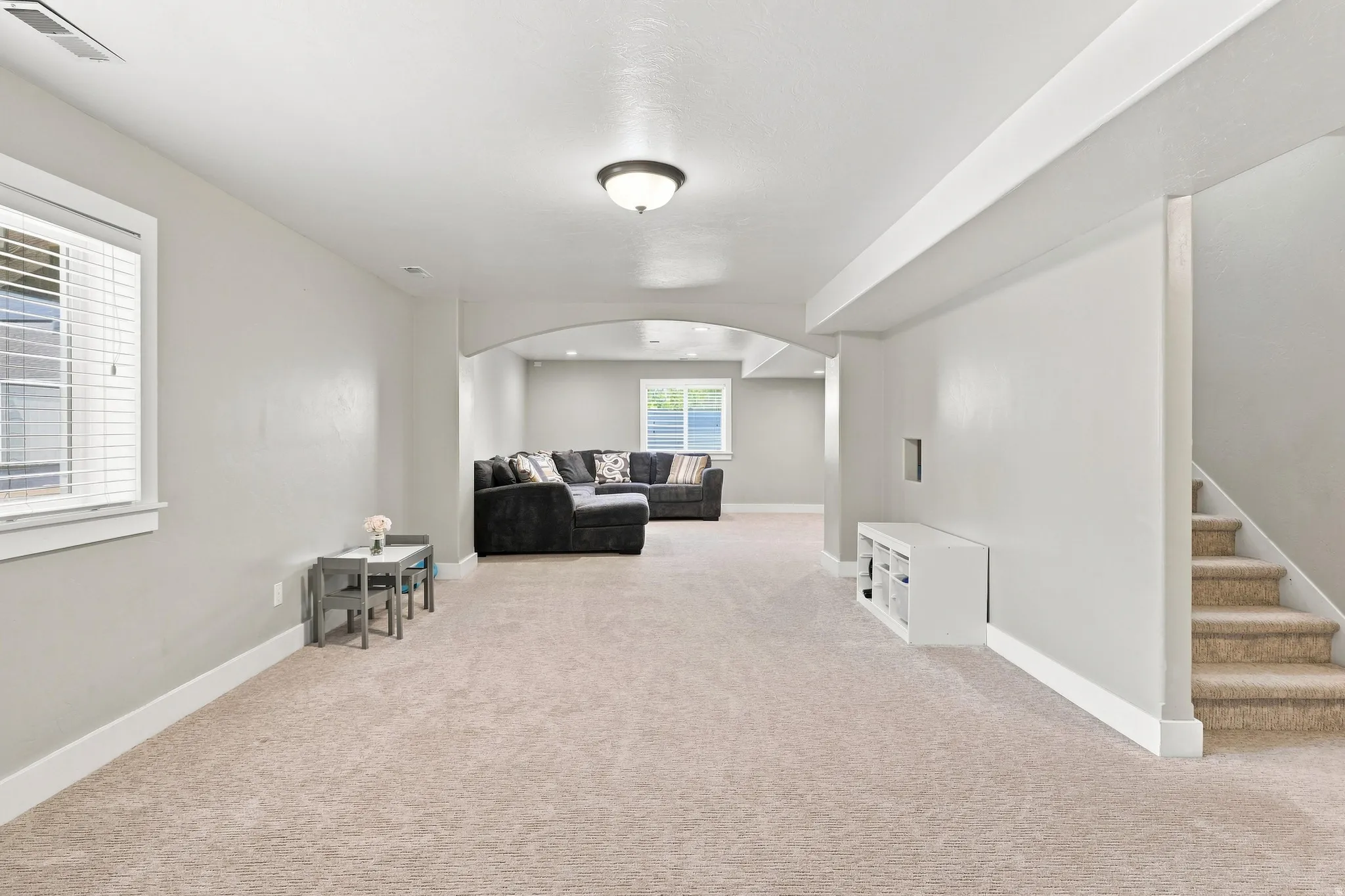 Spacious carpeted room featuring recessed lighting, a window with blinds, and an arched doorway