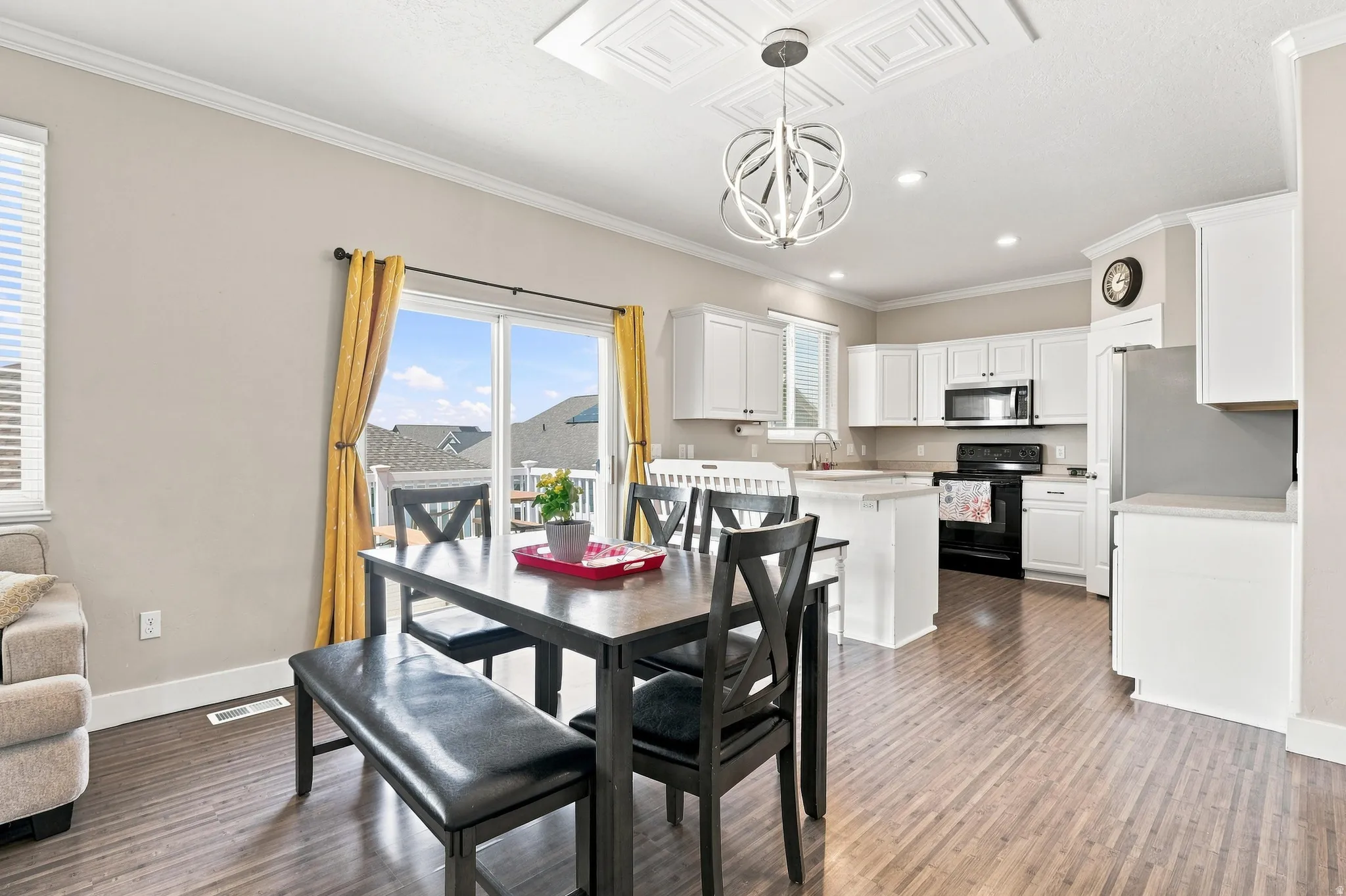 Wood-finish flooring, white cabinetry, integrated stainless steel appliances, recessed lighting, and a decorative ceiling light fixture