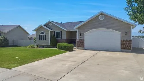 Exterior featuring tan siding, brick accents, a two-car garage, and a concrete driveway