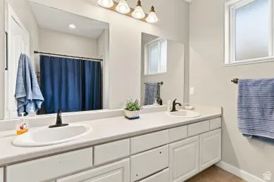Dual vanity with integrated sinks, ample countertop space, white cabinetry, and a large wall-mounted mirror