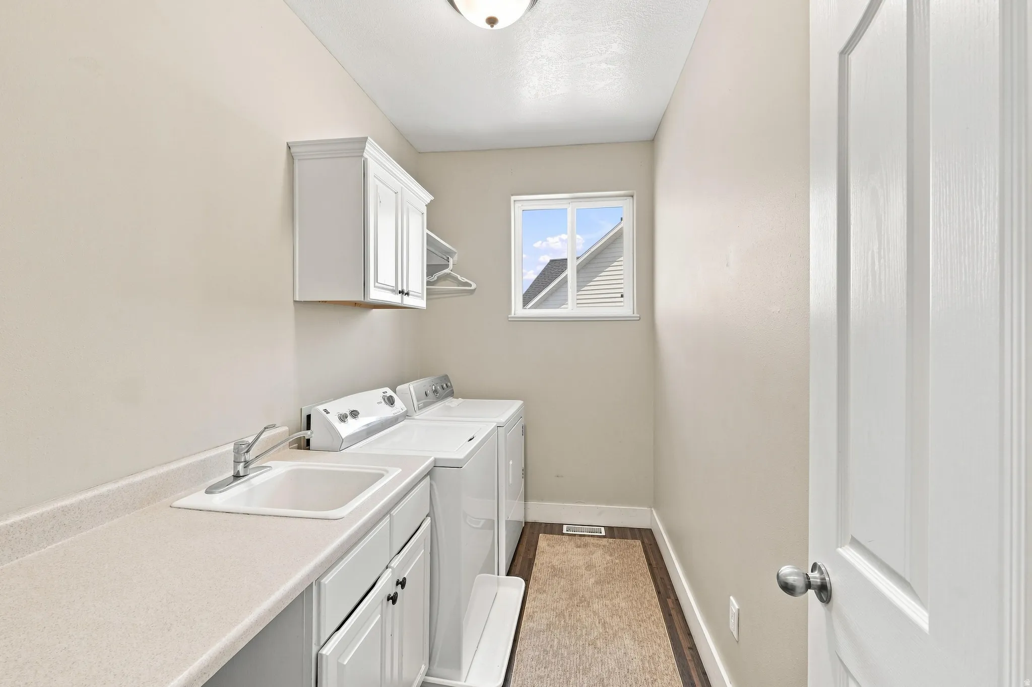 Laundry room featuring a utility sink, white cabinetry, a window, and wood-finish flooring