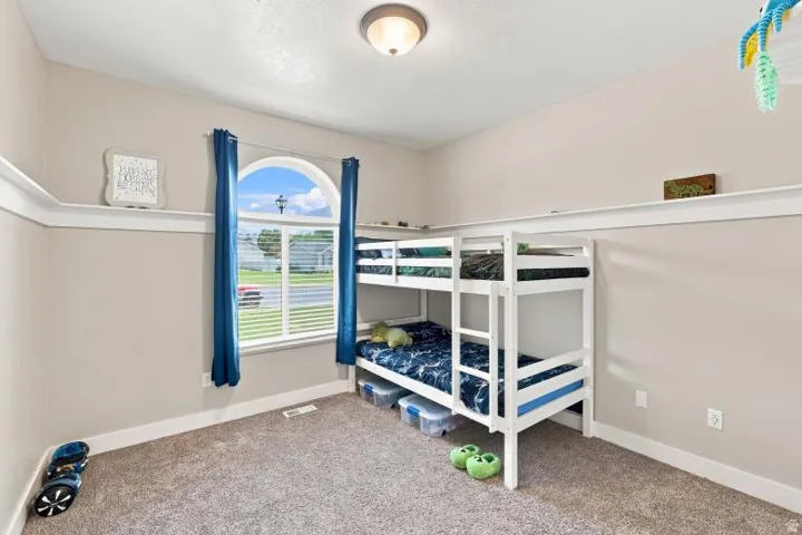 Arched window with blinds and blue drapery, wall shelving, neutral wall paint, and carpeted flooring