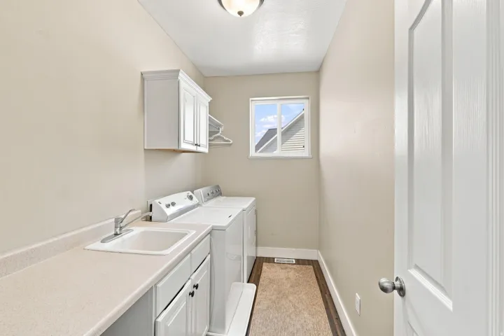 Dedicated laundry area featuring a utility sink, white cabinetry, a window, and wood-finish flooring