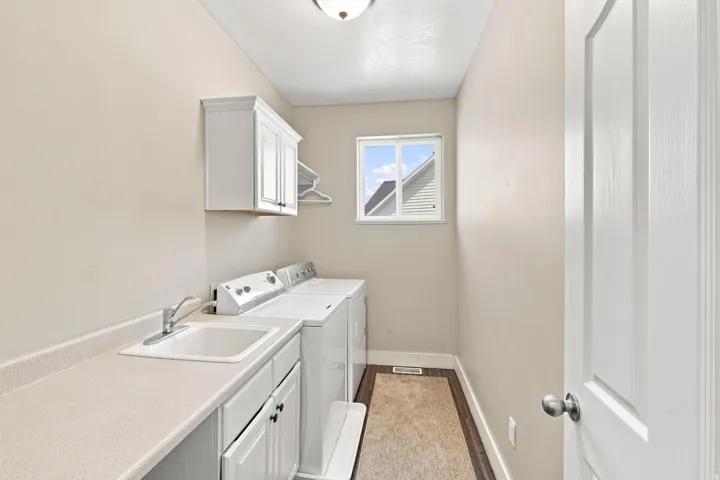 Laundry room featuring a utility sink, white cabinetry, a window, and wood-finish flooring