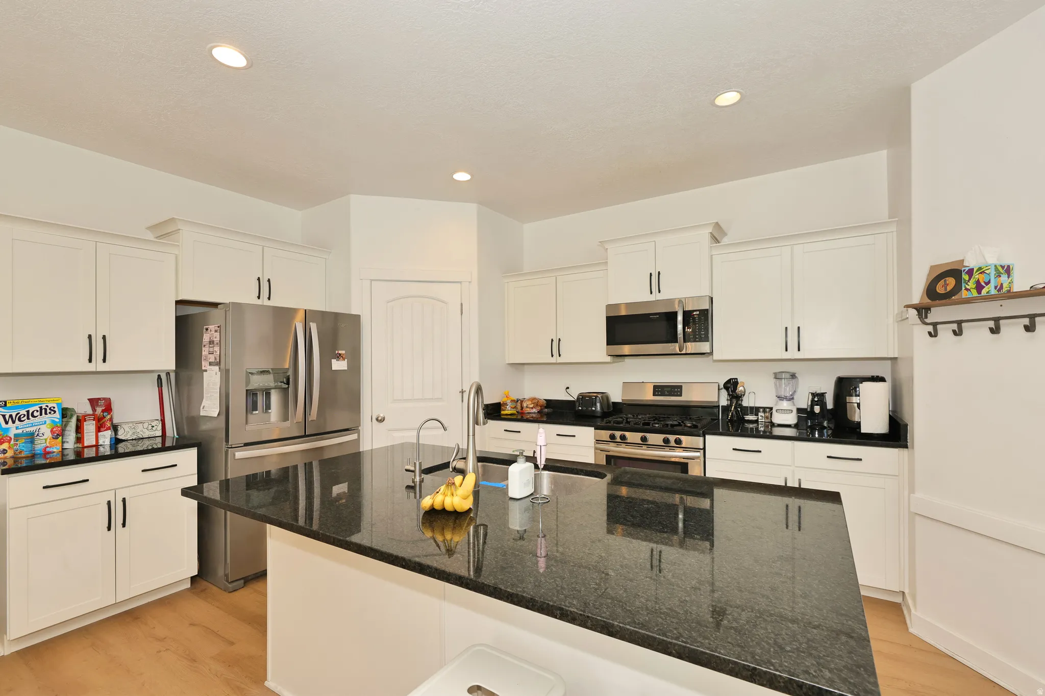 White cabinetry with dark hardware, stainless steel appliances, dark stone countertops, wood-finish flooring, and recessed lighting