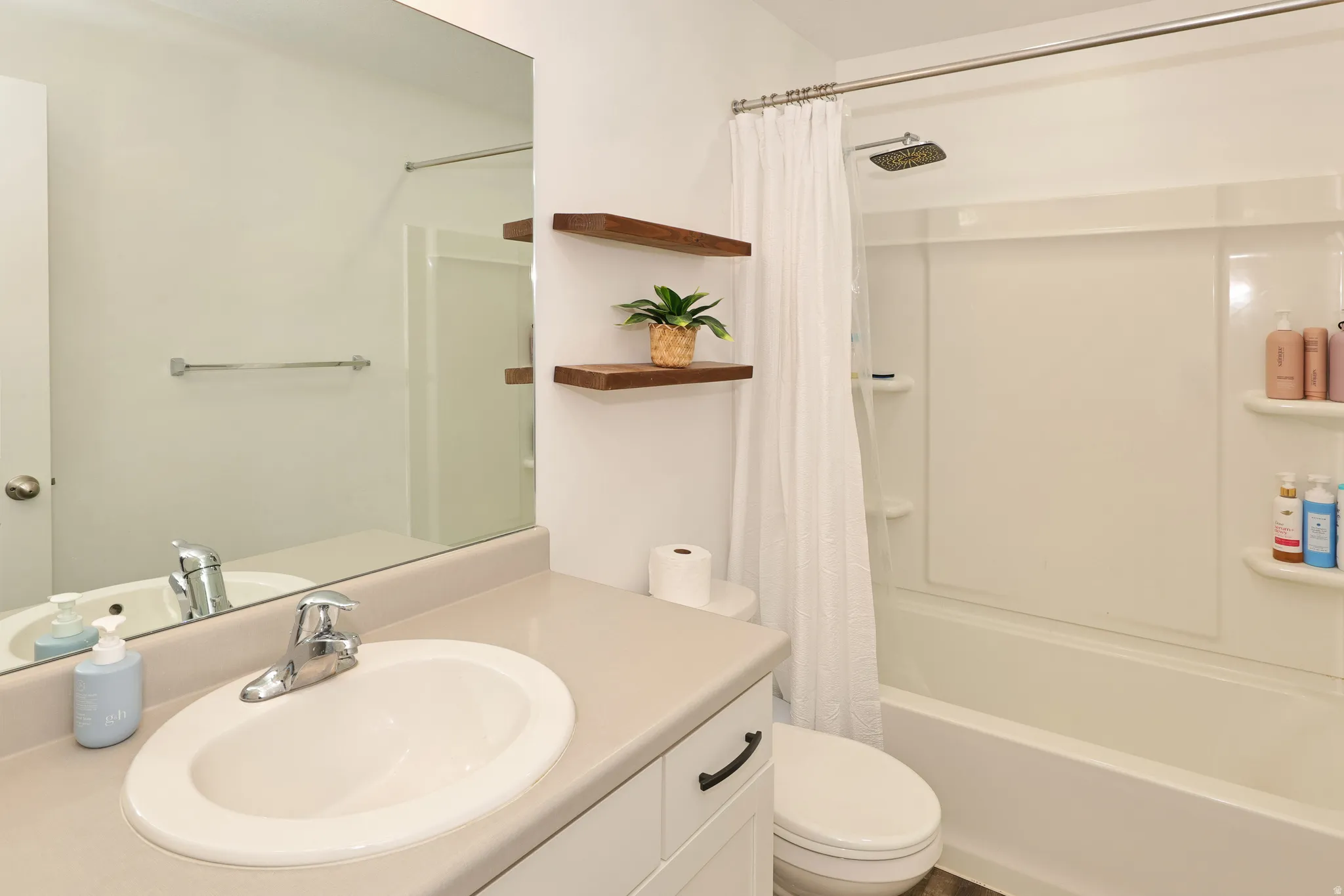 Bathroom featuring a vanity with an integrated sink, polished chrome faucet, built-in shelving, and a full-size bathtub with shower combination