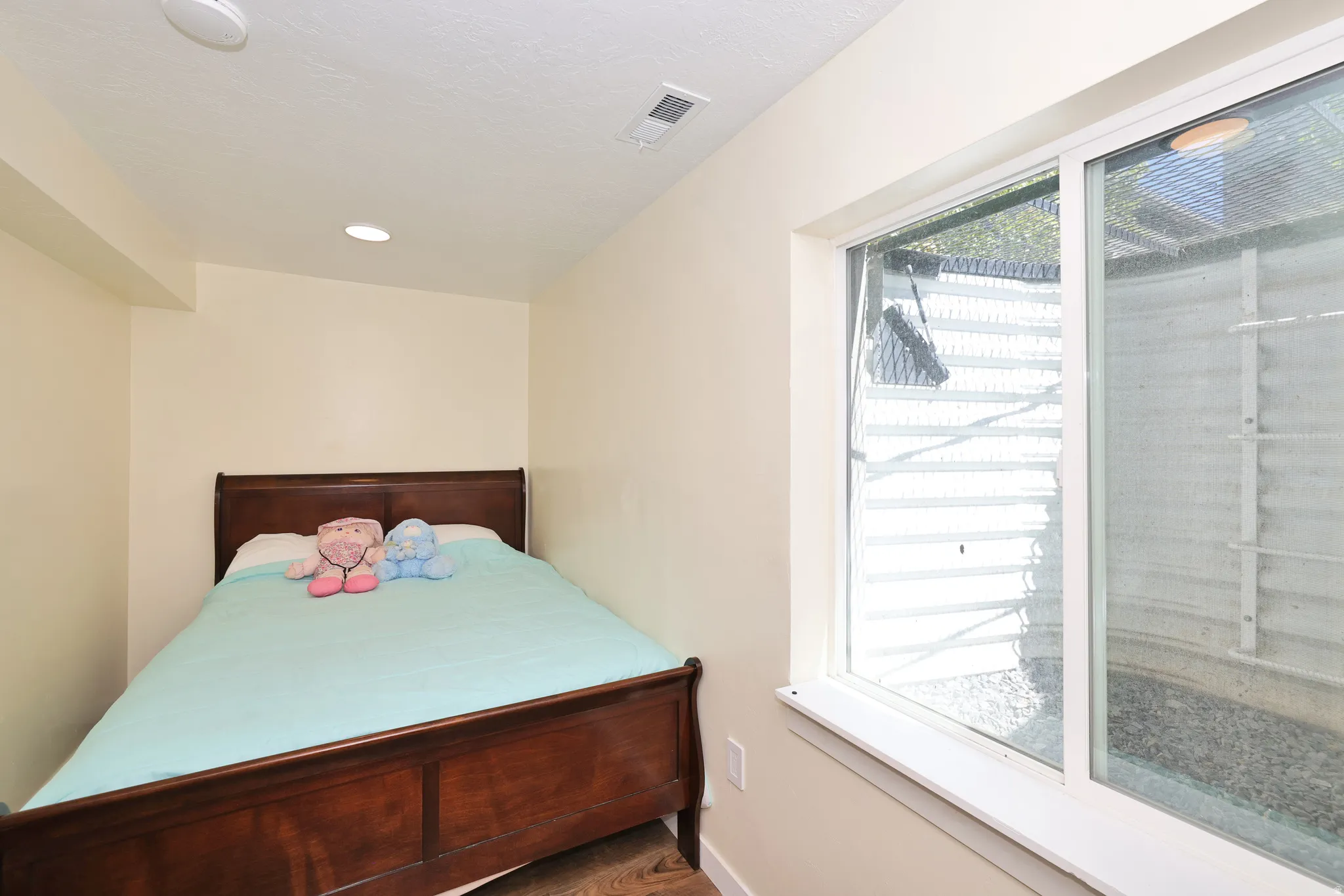 Wood-finish flooring, recessed ceiling lighting, light-toned wall paint, and a sliding window with a window well