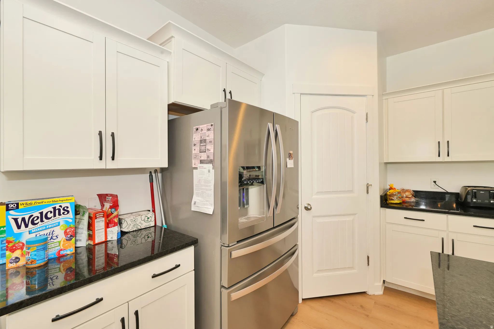 White shaker-style cabinetry with matte black hardware, dark countertops, and wood-finish flooring