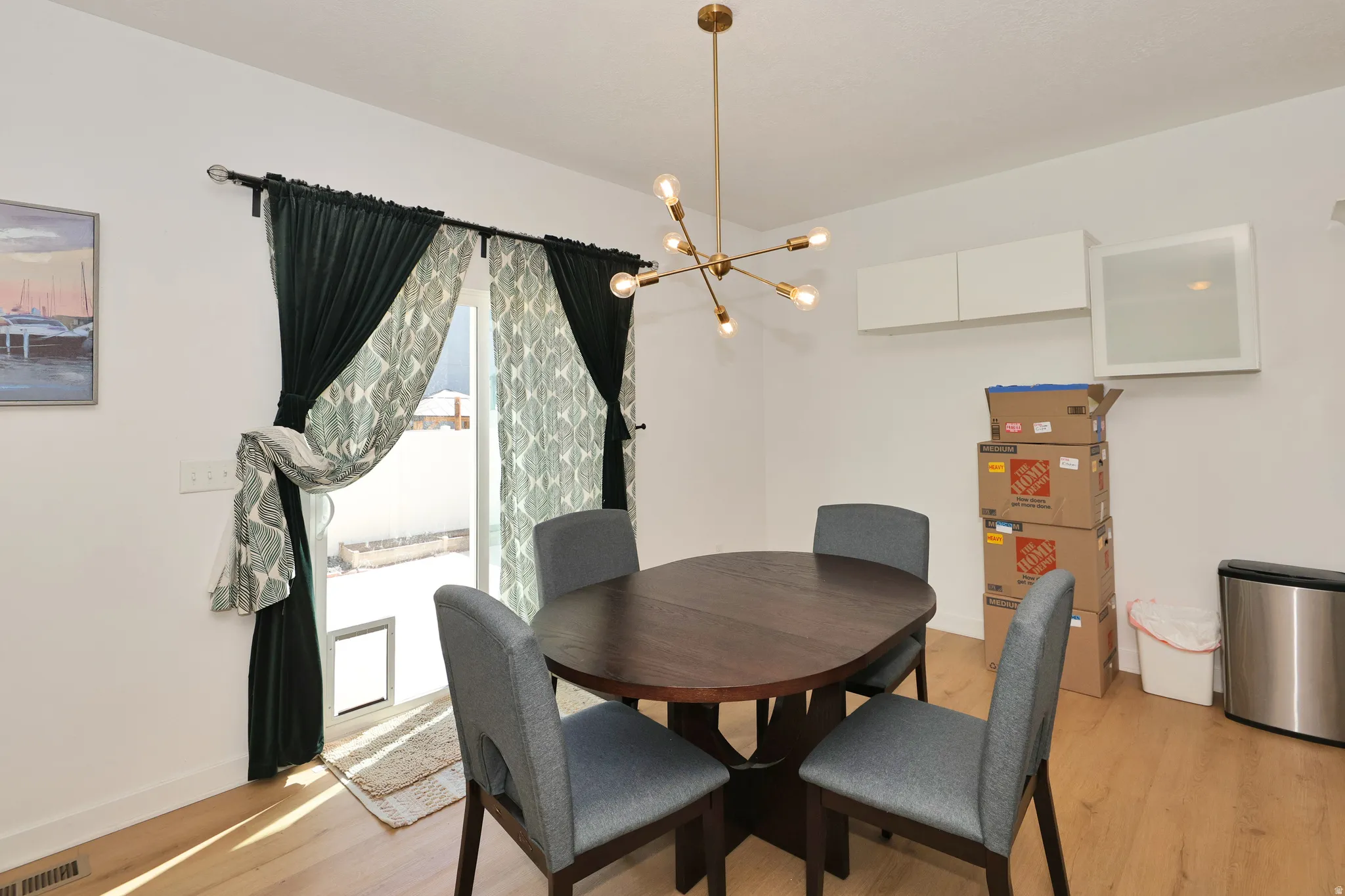 Wood-finish flooring, modern brass sputnik chandelier, white wall-mounted cabinetry, and a sliding glass door