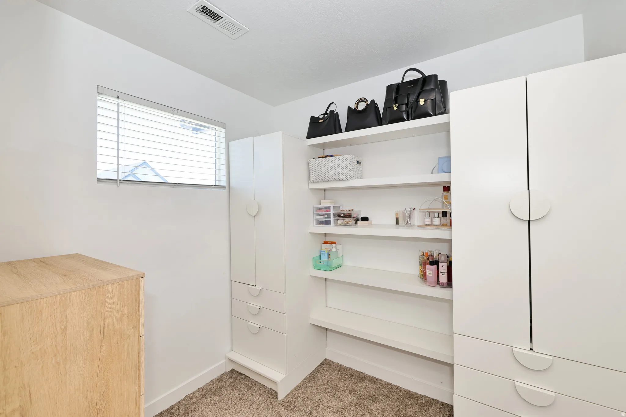 Built-in shelving, white cabinetry with round pull hardware, and window with blinds