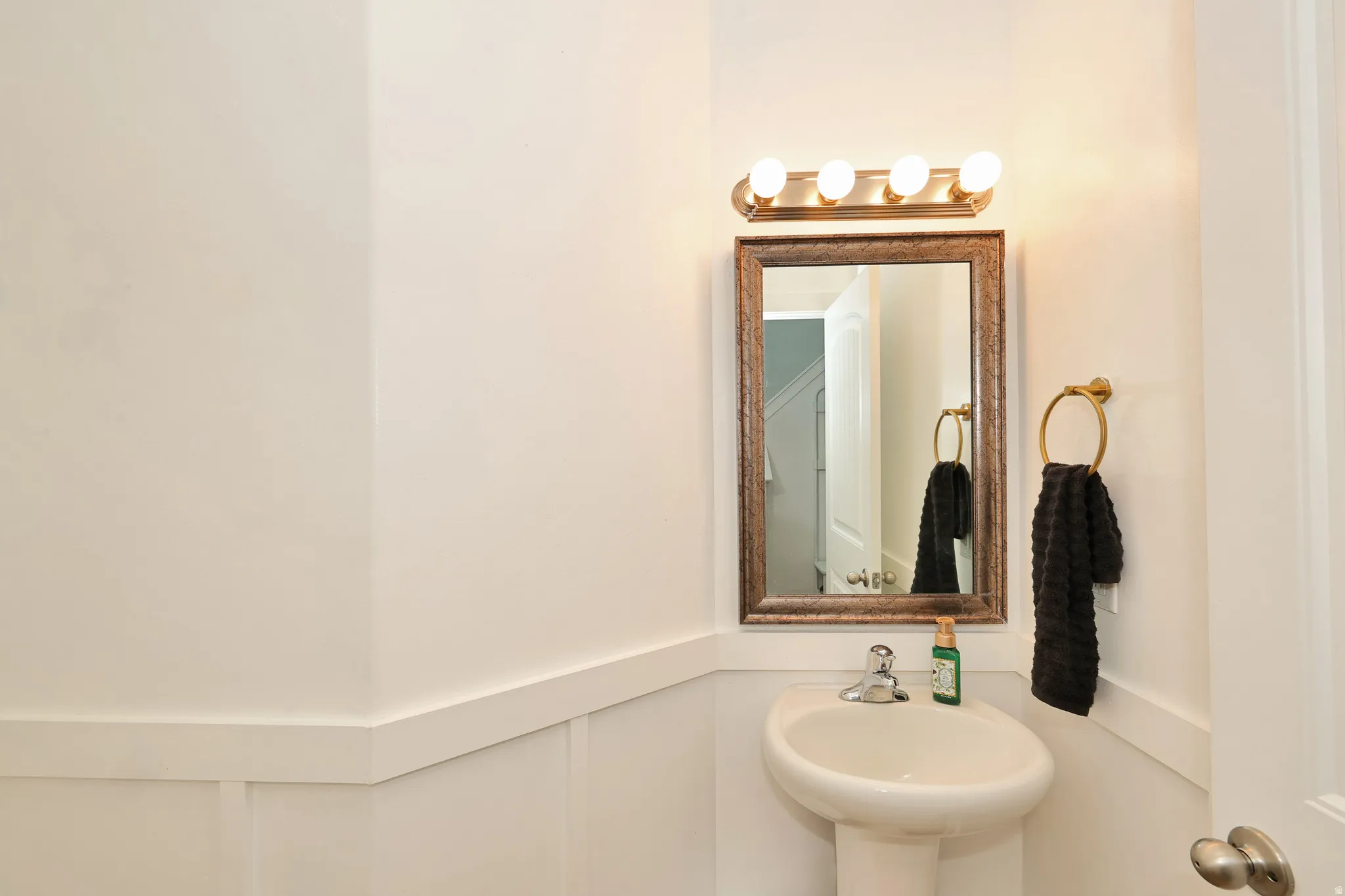 Pedestal sink with chrome faucet, framed mirror, and wall-mounted light fixture