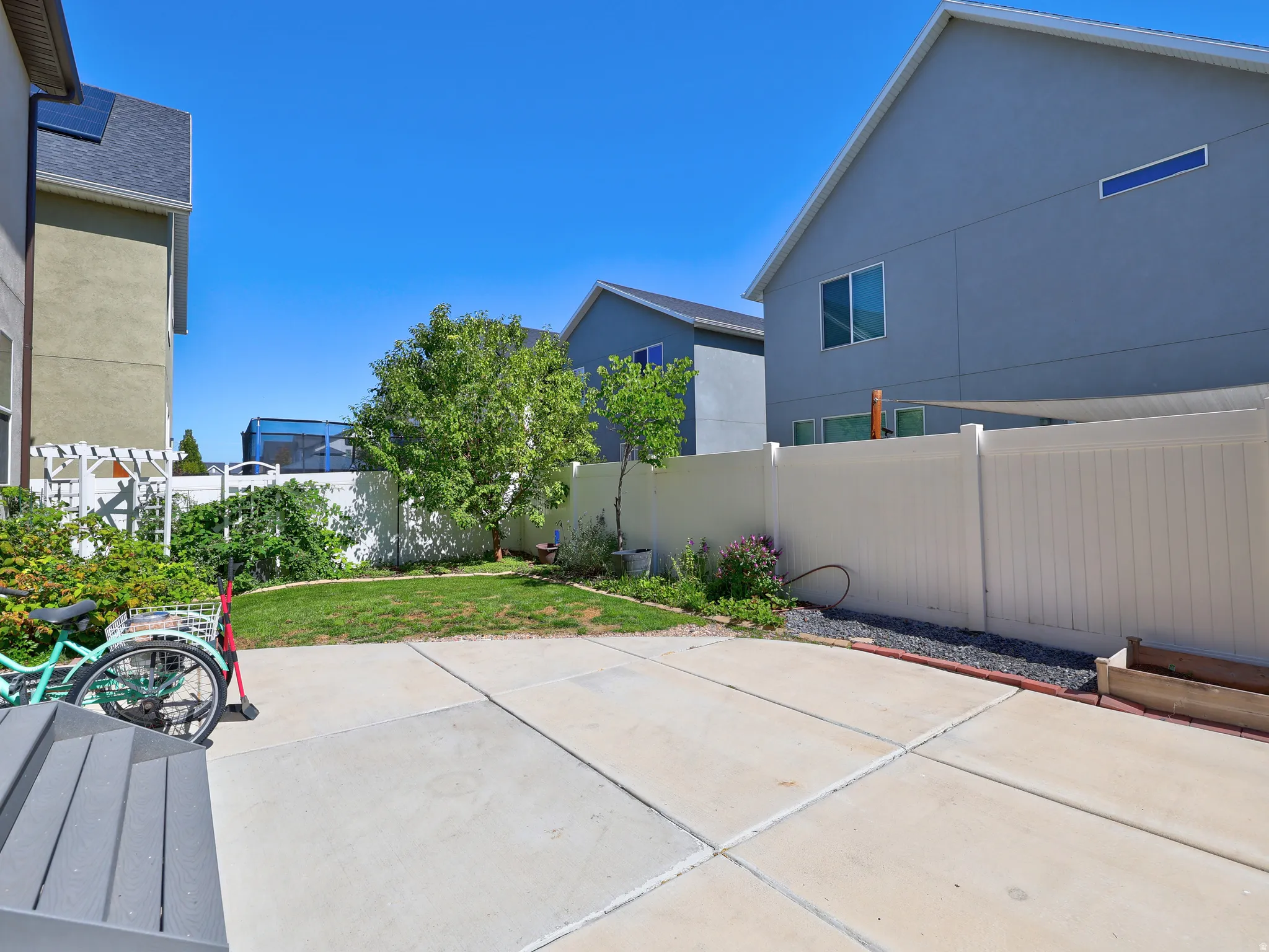 Paved patio area, white privacy fencing, established trees, and a garden bed