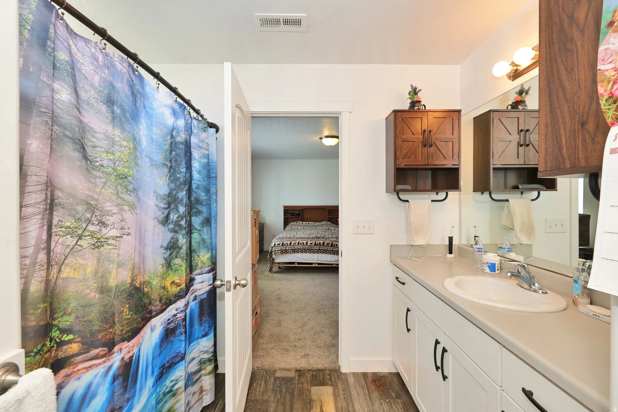 Vanity with white cabinetry and dark hardware, set against wood-finish flooring