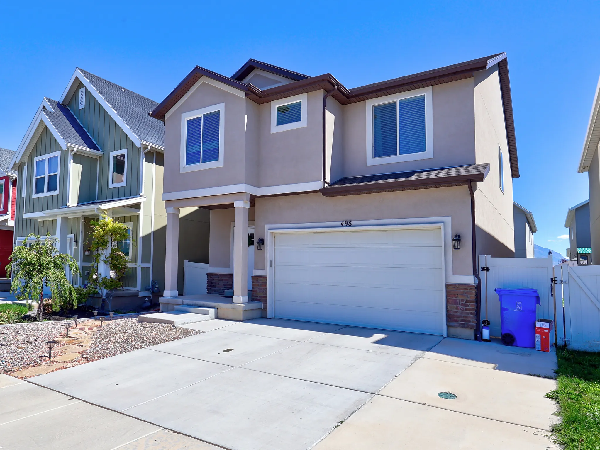 Stucco exterior with stone accents, covered front entry, attached garage, and mature landscaping