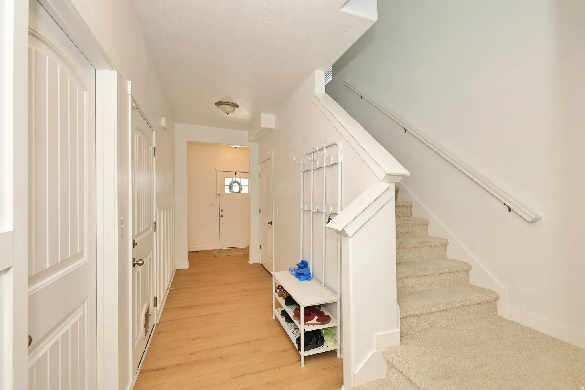 Entryway with wood-finish flooring, white panel doors, and a carpeted staircase with a white railing
