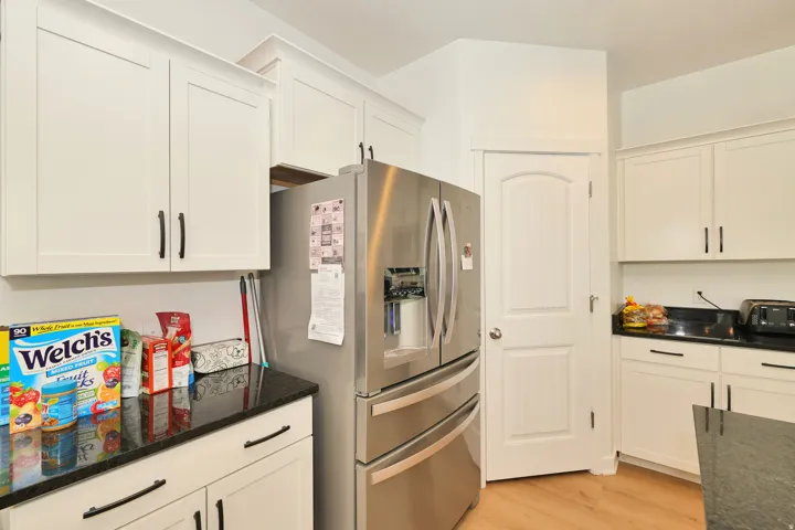 White shaker-style cabinetry with matte black hardware, dark countertops, and wood-finish flooring
