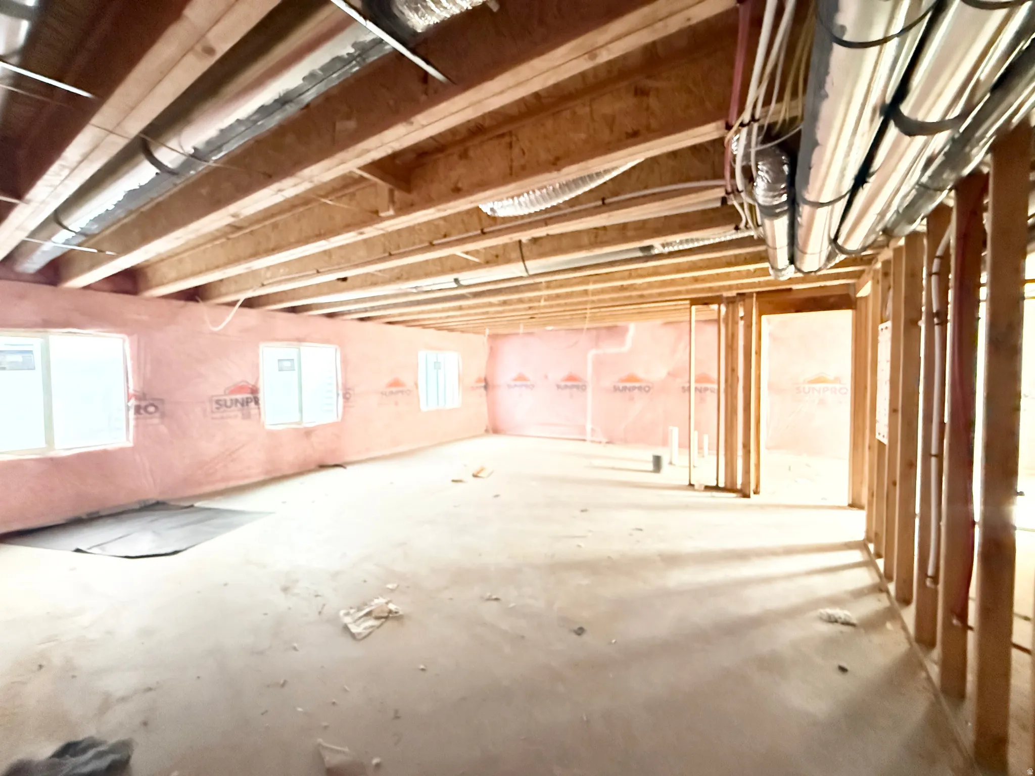 Unfinished lower level featuring exposed wood joists, utility piping, framed interior walls, multiple windows, and insulation