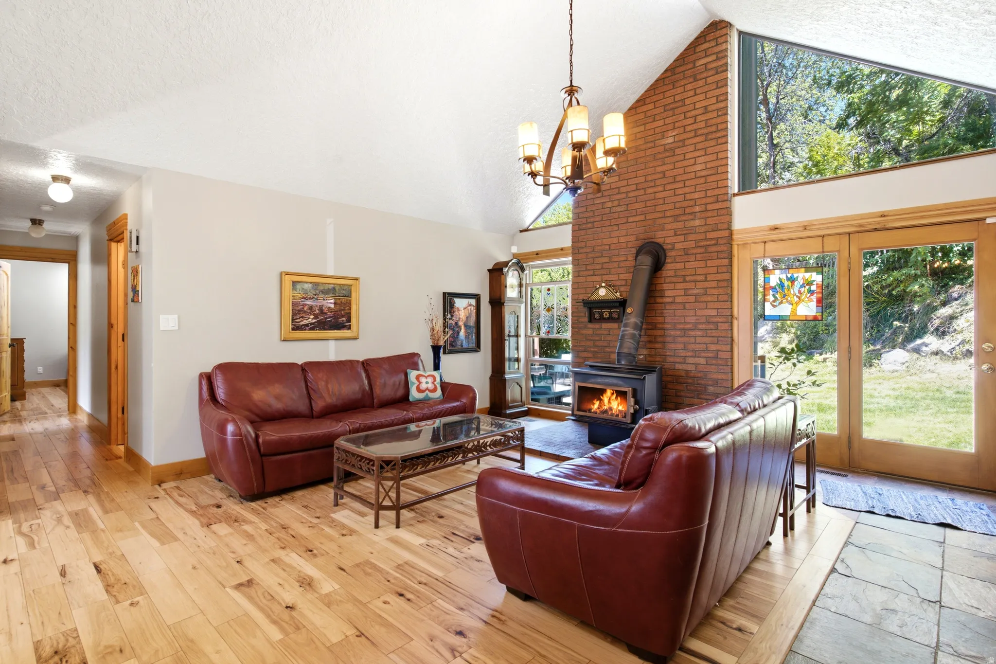 Vaulted ceiling, wood-finish flooring, brick-clad accent wall, wood-burning stove, and wood-framed glass patio doors