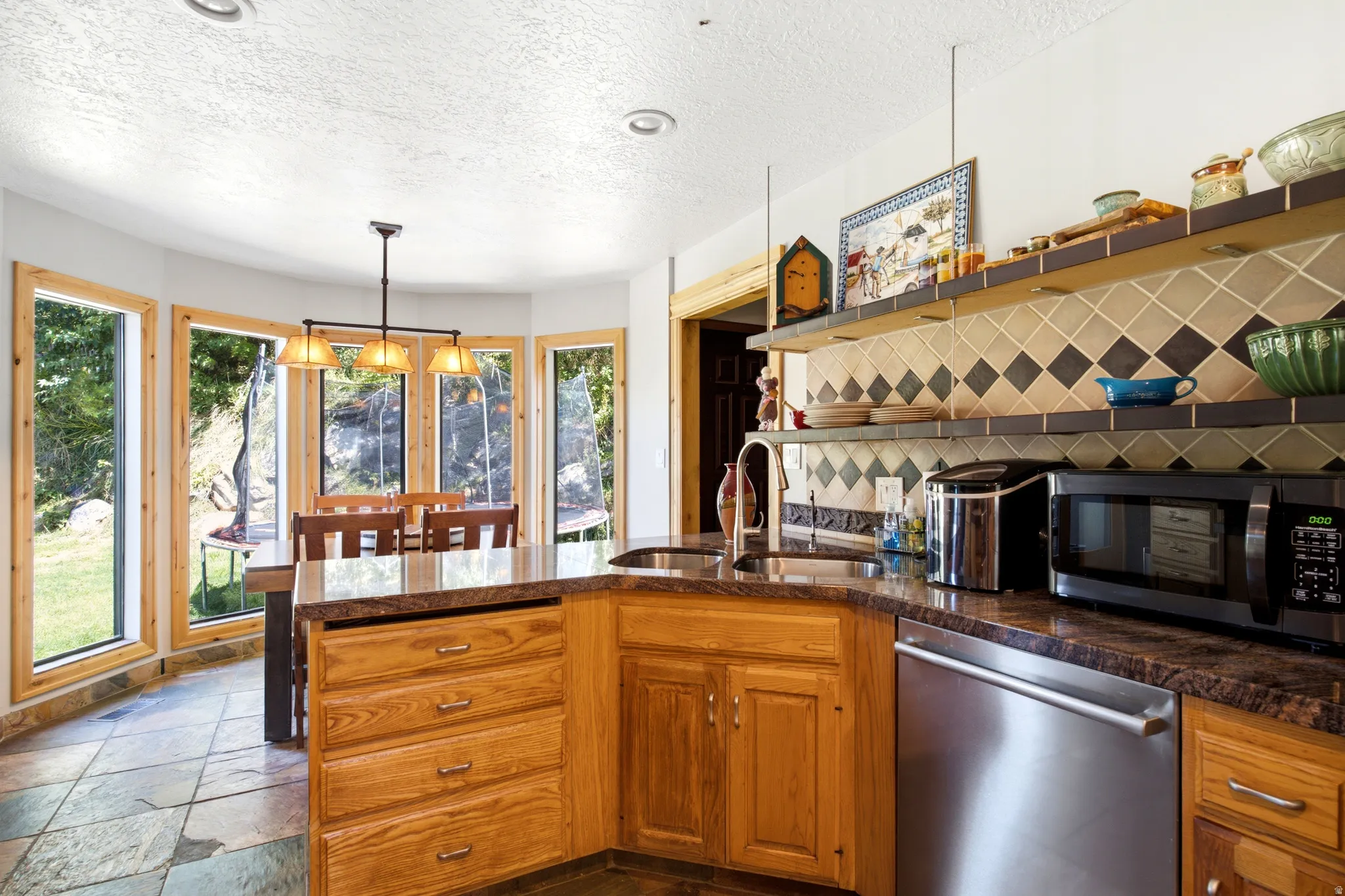 Wood cabinetry with stone countertops, stainless steel dishwasher, tile backsplash, open shelving, and slate tile flooring